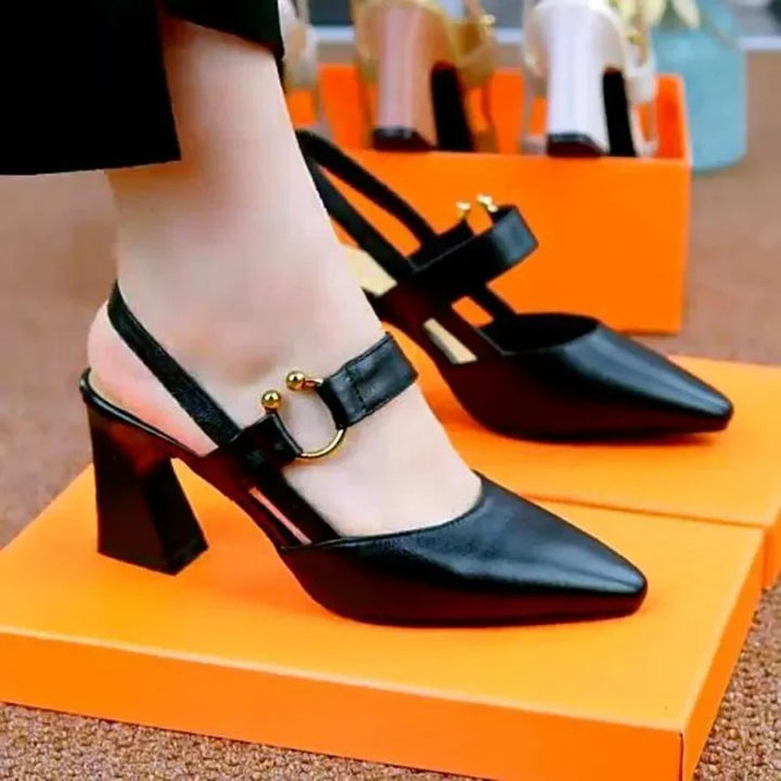 Black high-heeled shoes with gold buckles on an orange shoe box.